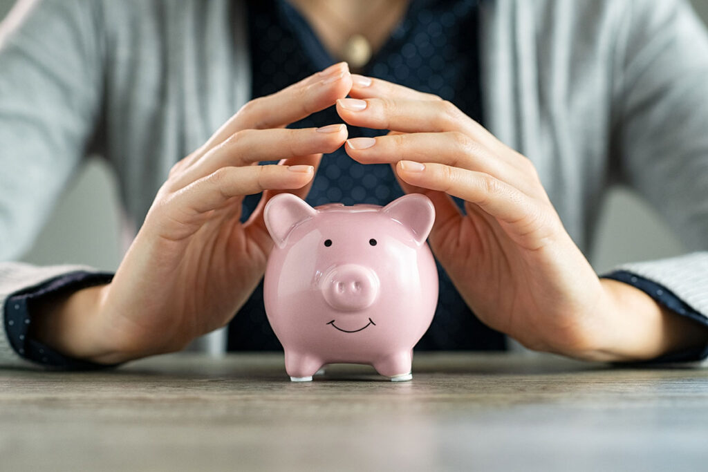Close up of hands of woman protecting piggy bank for saving.